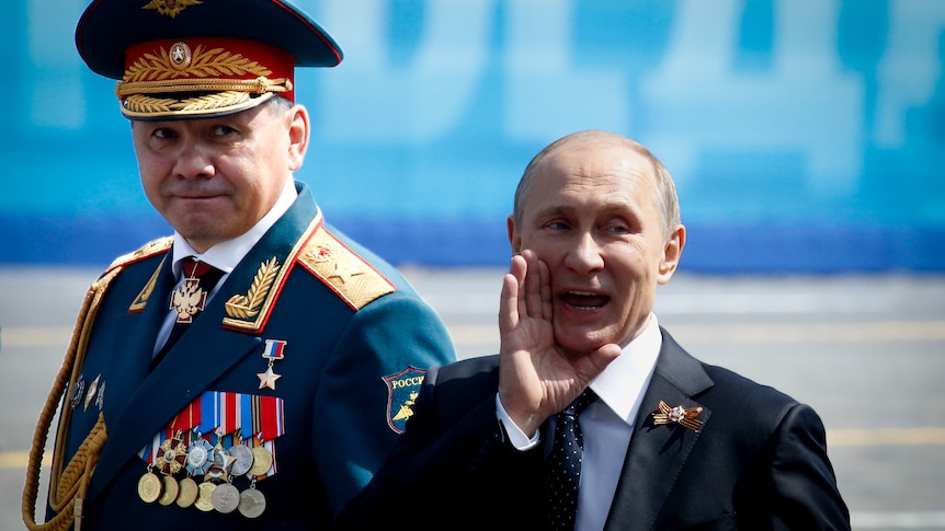 Vladimir Putin smiling and gesturing while walking with Sergei Shoigu