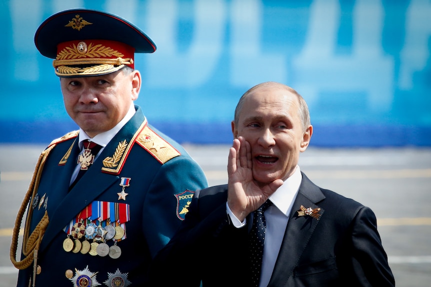 Vladimir Putin smiling and gesturing while walking with Sergei Shoigu