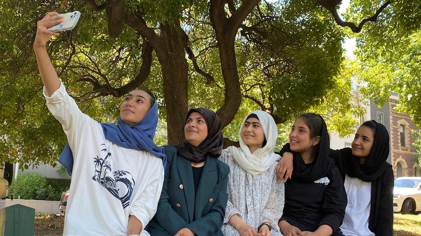 Five Afghanistan women's cricketers take a selfie while sitting on a bench in Melbourne.