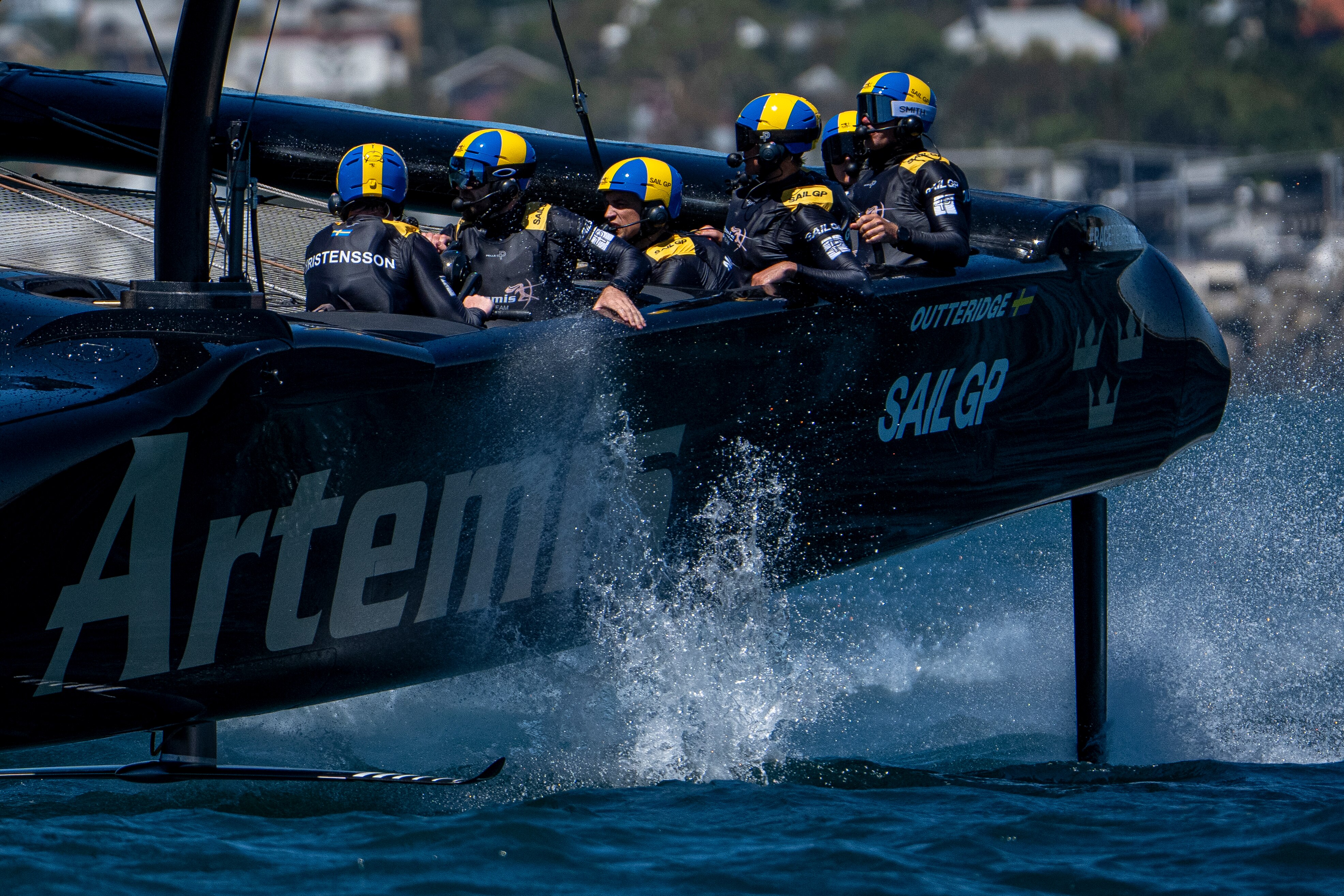 Close de uma tripulação de marinheiros a bordo de um catamarã de alta velocidade com a palavra 'Artemis' escrita. 