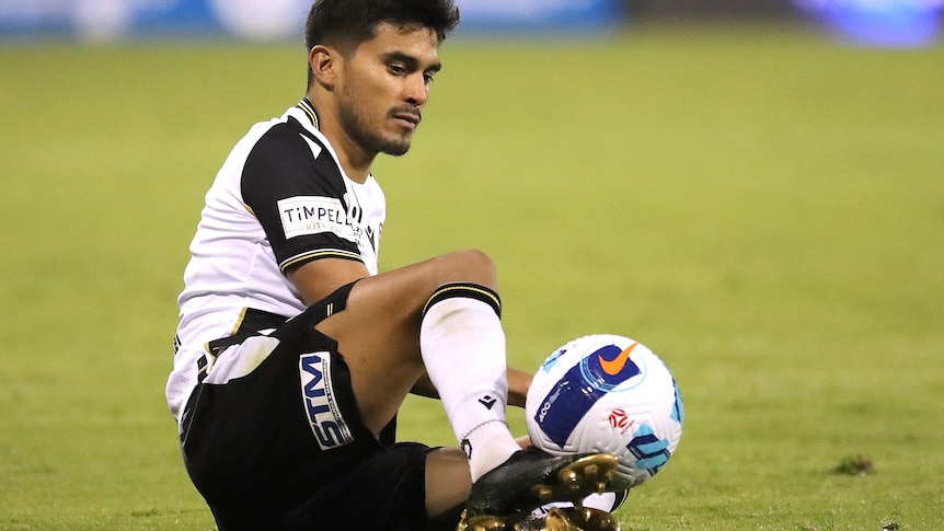 A footballer sat on the ground with a ball at his feet