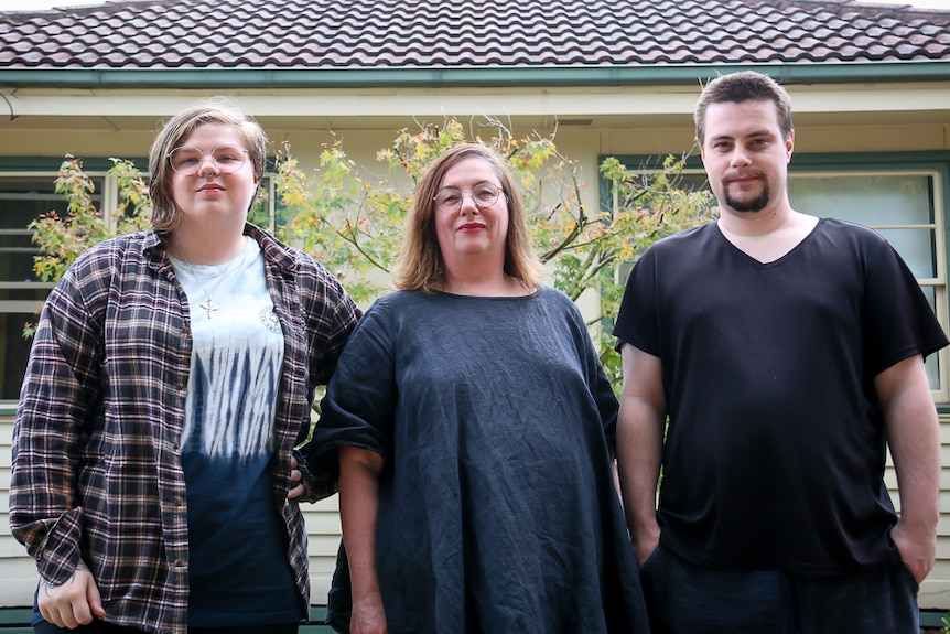 Jacki Whittaker stands between her two adult children in front of their contaminated home in Melbourne