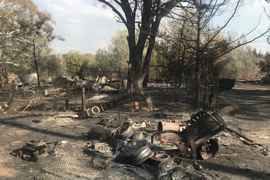 A rural yard blackened by fire with metal remains of equipment and buildings.