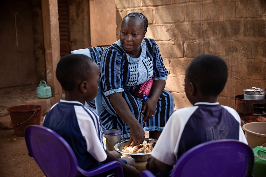 Woman in Africa outside, preparing lunch for her two children.