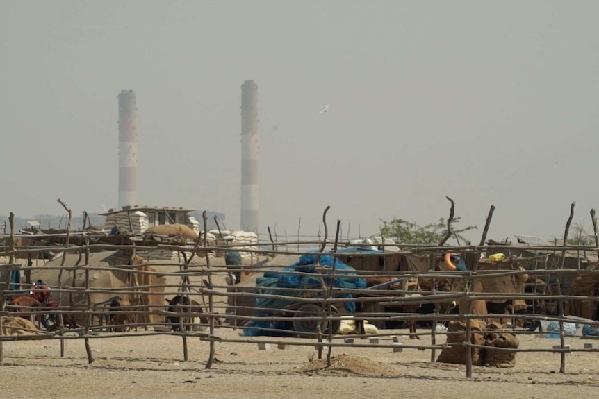 A fishing village sits in the foreground in front of two striped poles from the electricity plant nearby.