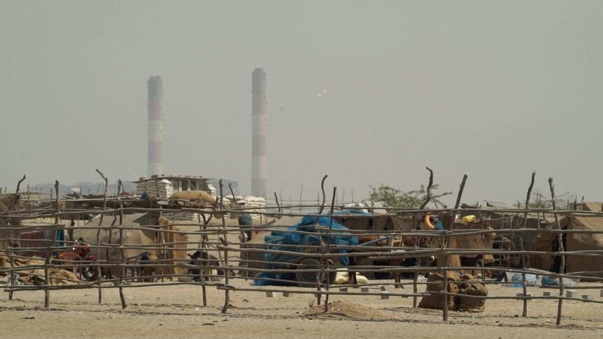 A fishing village sits in the foreground in front of two striped poles from the electricity plant nearby.
