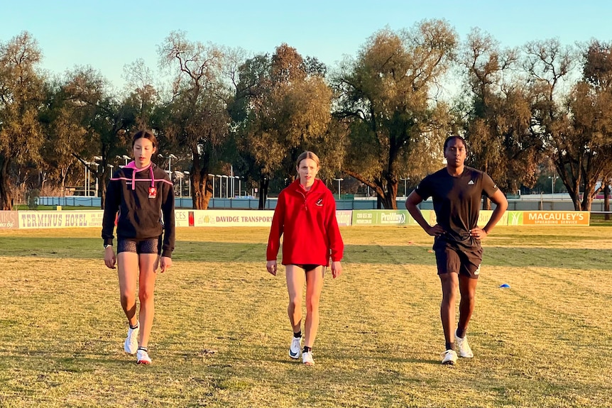 Three young athletes, including two girls and a boy, walking across a field towards the camera.