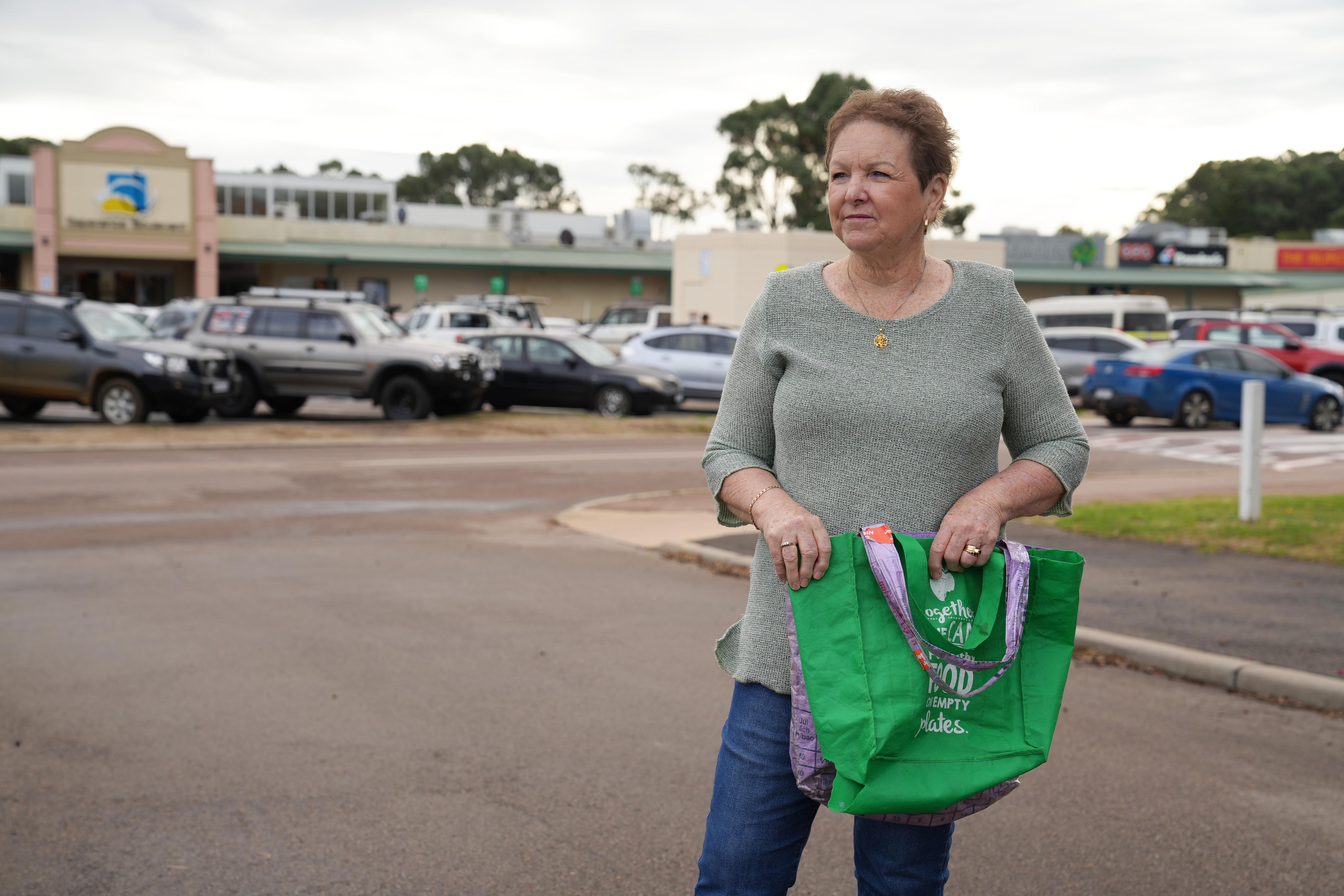 She holds two shopping bags and stands by a supermarket carpark