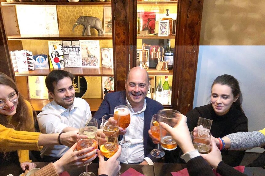 Nicola Zingaretti clinking glasses with a group of people at a bar in Milan
