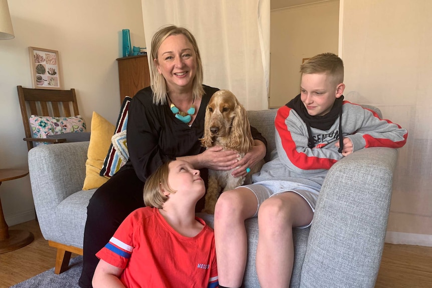 A family of a mother, two children and a dog sit on a couch.