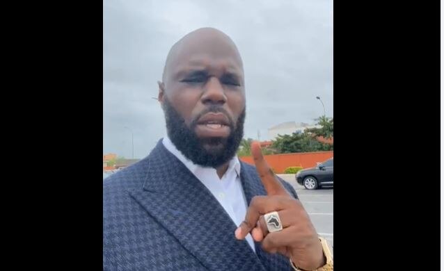 A screen capture from a Facebook video shows a man in a tweed suit, pointing at the camera. 