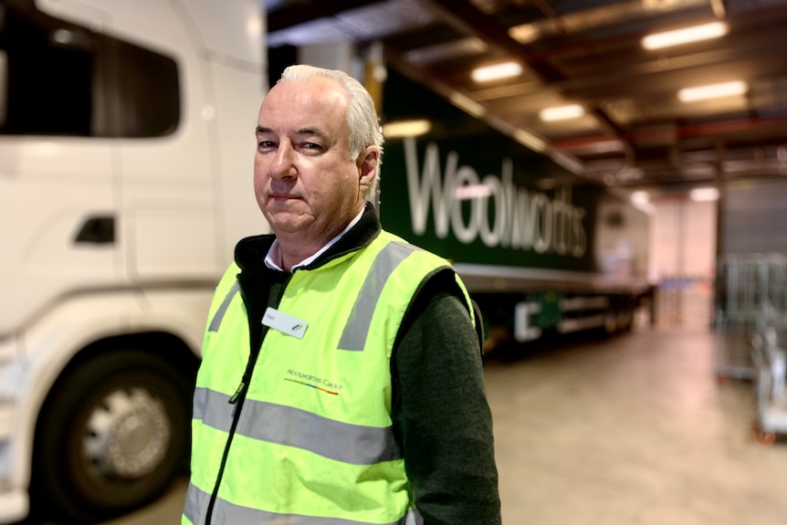 A man in a high-vis vest stands in front of a Woolworths truck