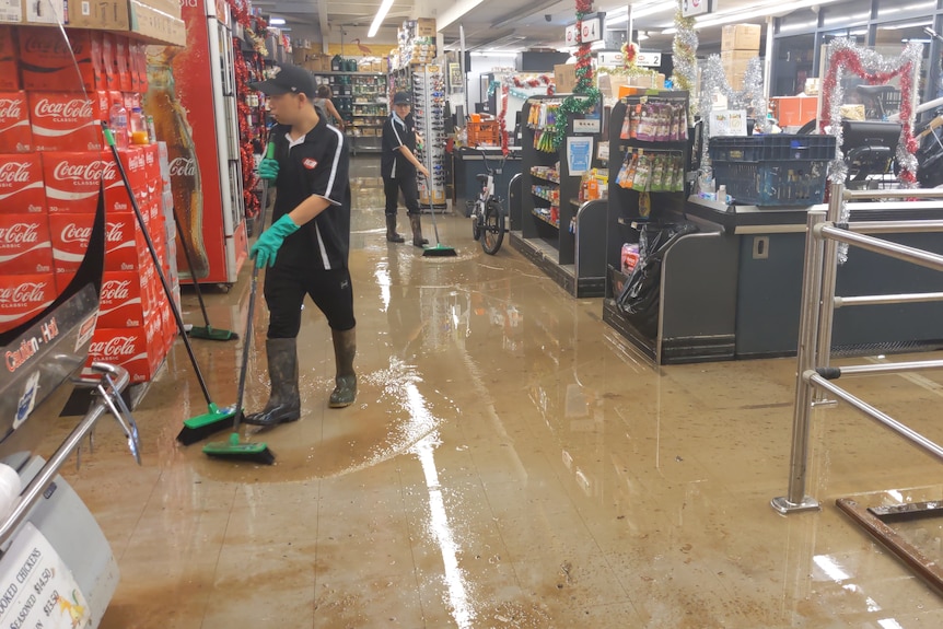 Staff at the Tarunda IGA in Fitzroy Crossing using brooms to push floodwater out of the shop.