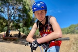 A boy wearing a blue helmet leaning on the handles of a BMX bike