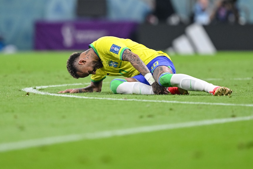 Neymar está tirado en el césped agarrándose el tobillo derecho.