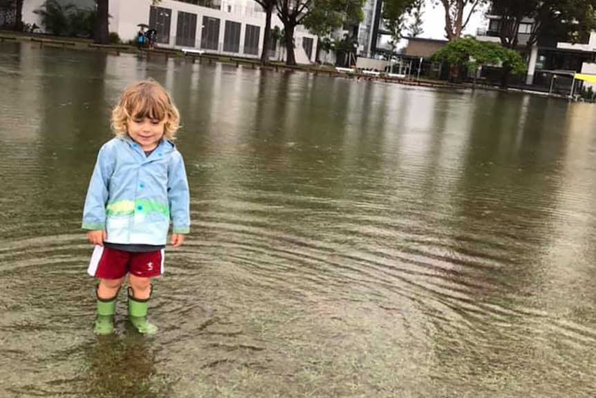 A little boy standing in gumboots on a flooded oval