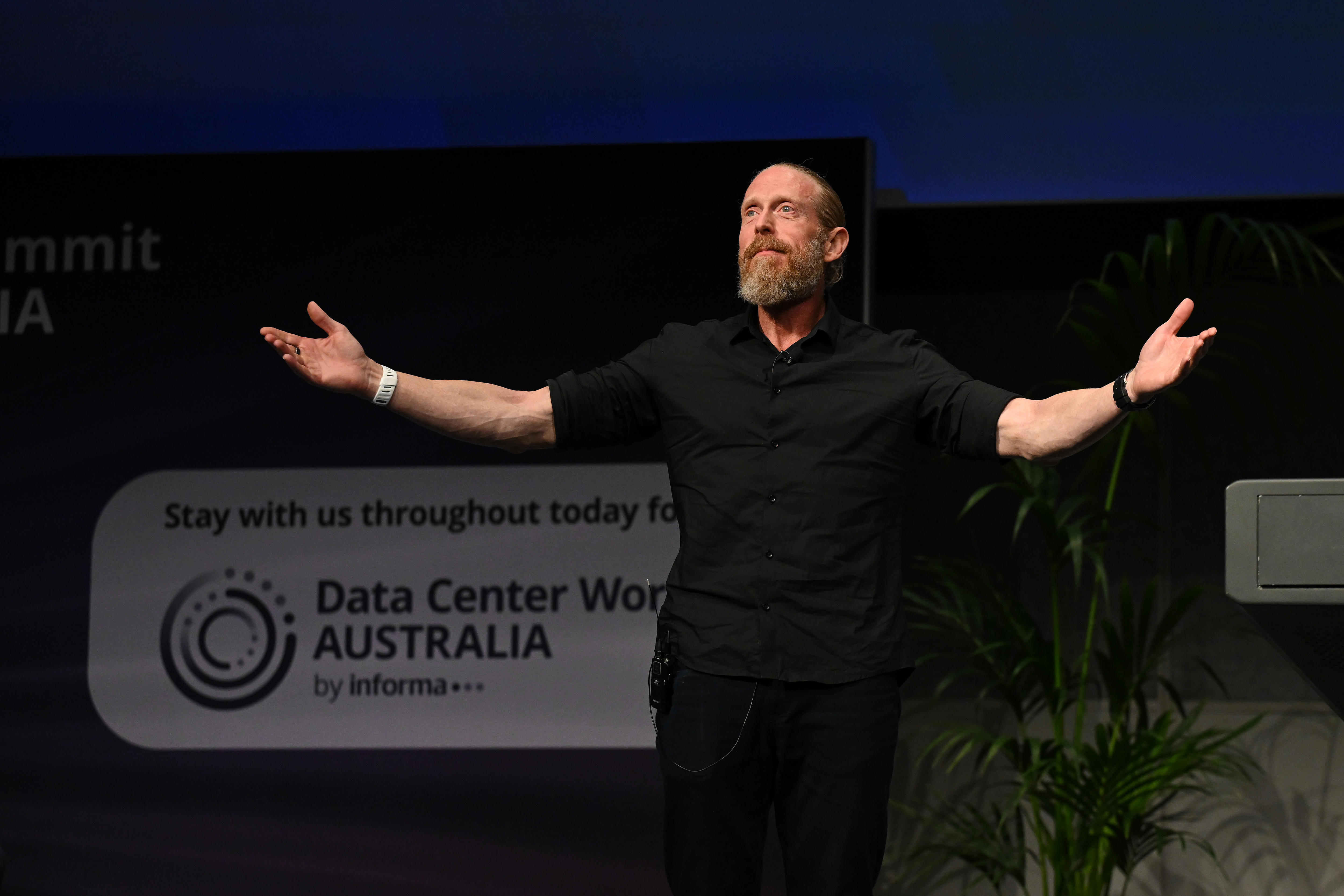 Craig Scroggie stands on stage, holding arms wide