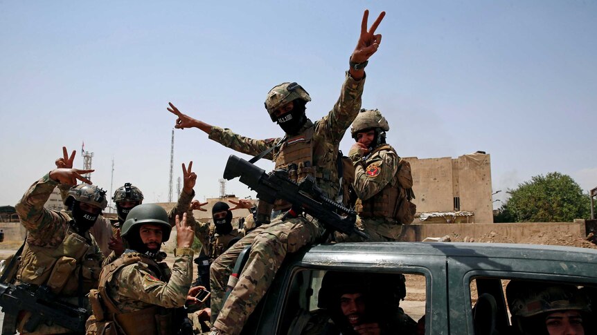 Members of Iraqi forces make a "V" sign as they arrive to take part in a victory celebration.