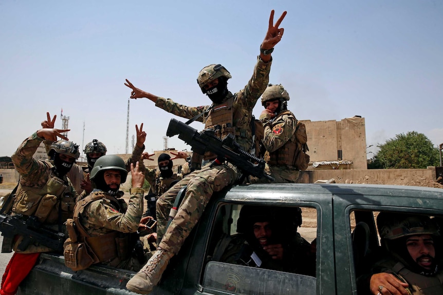 Members of Iraqi forces make a "V" sign as they arrive to take part in a victory celebration.