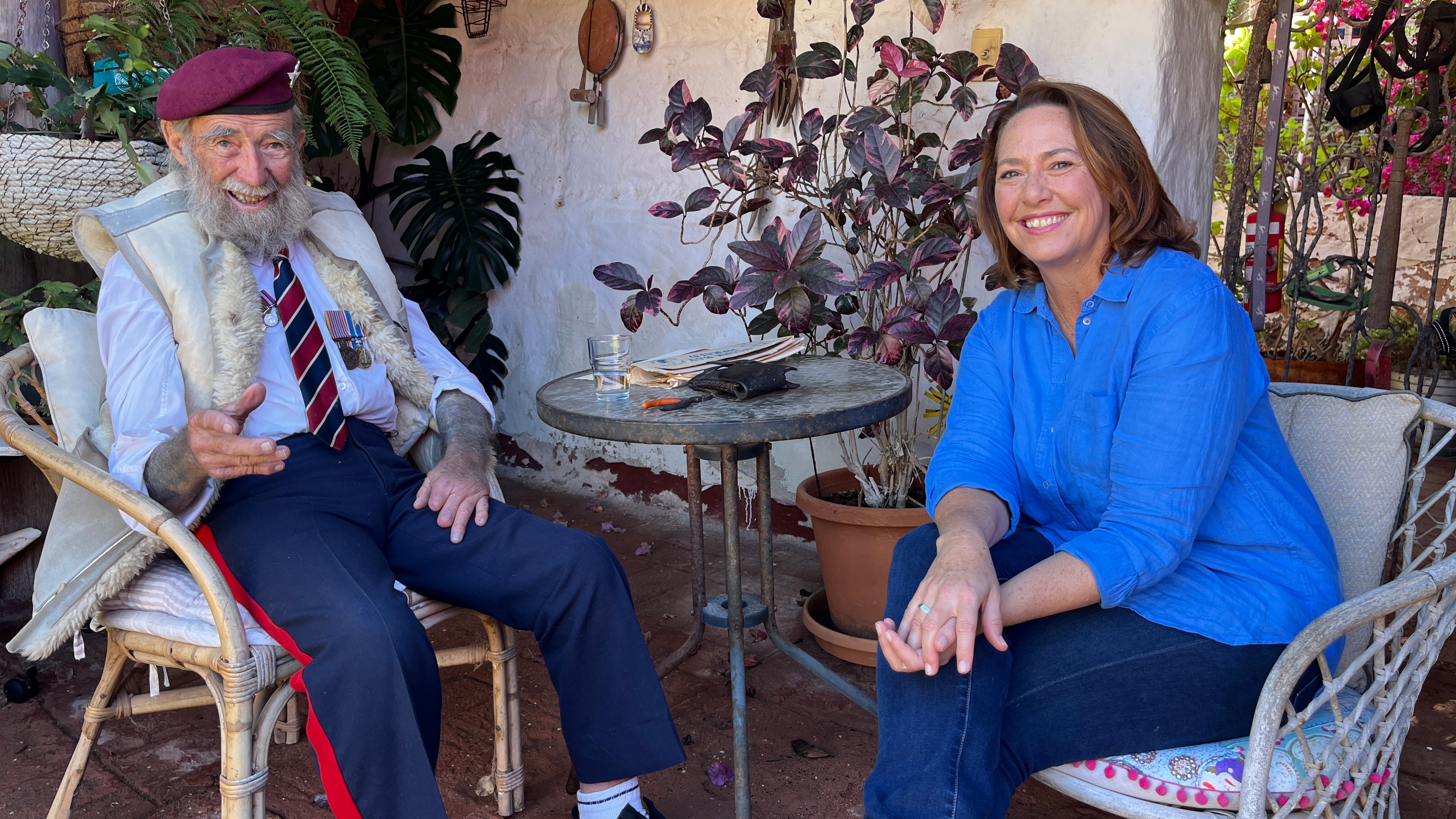 Un anciano está sentado en una silla frente a Lisa Millar, ambos sonriendo.