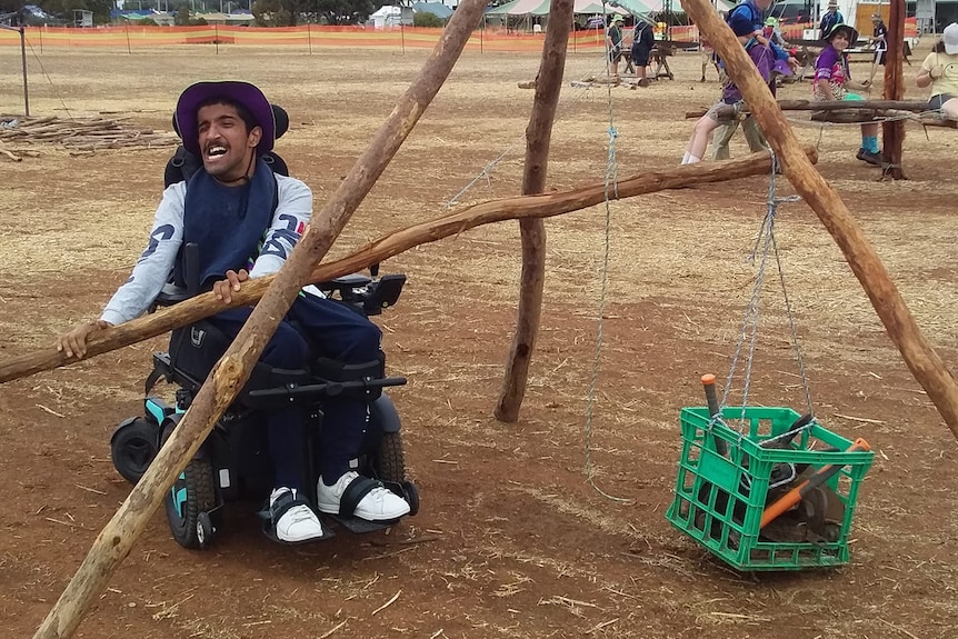 A man in a wheelchair wearing a hat, with a log of wood. 