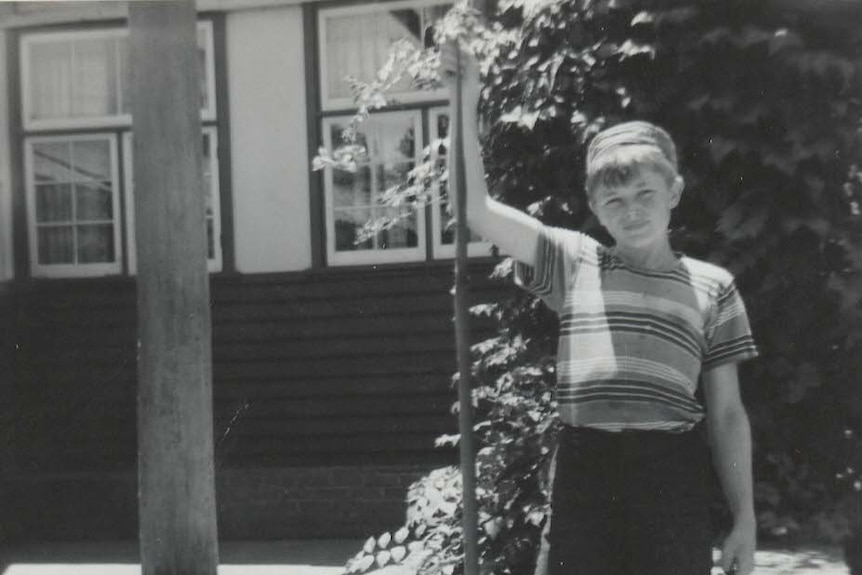 A black-and-white picture of Ric Hinch  about 10-years-old, in a striped T-shirt, holding a snake, outside a cottage