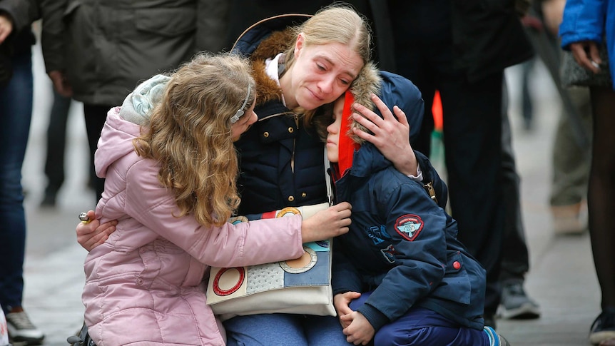 A woman consoles her children at a street memorial.