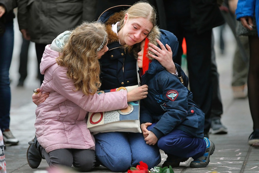 A woman consoles her children at a street memorial.
