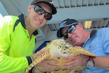Dive boat crew members hold Harry the hawksbill turtle moments before his release back into the wild.