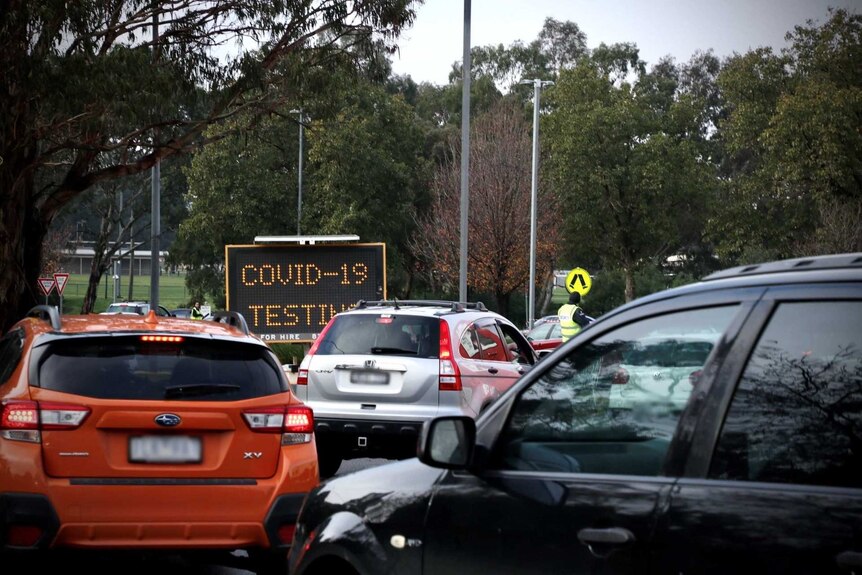A line of cars near a sign with COVID-19 testing on it.