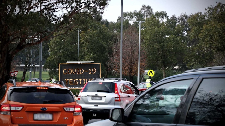 A line of cars near a sign with COVID-19 testing on it.