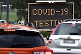 A line of cars near a sign with COVID-19 testing on it.