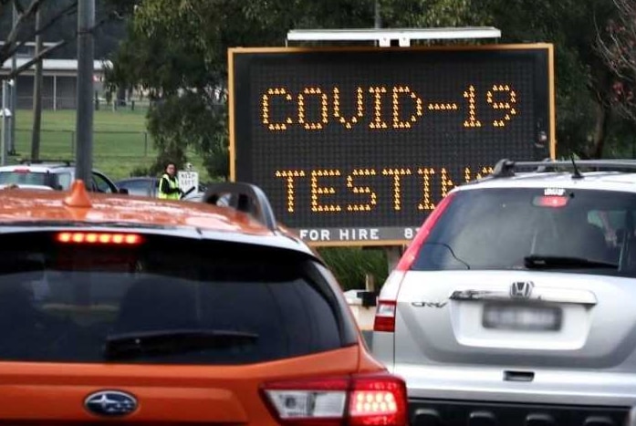 A line of cars near a sign with COVID-19 testing on it.