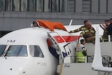 A man in lying on top of a plane face down with an orange blanket over him there are police standing next to him on stairs