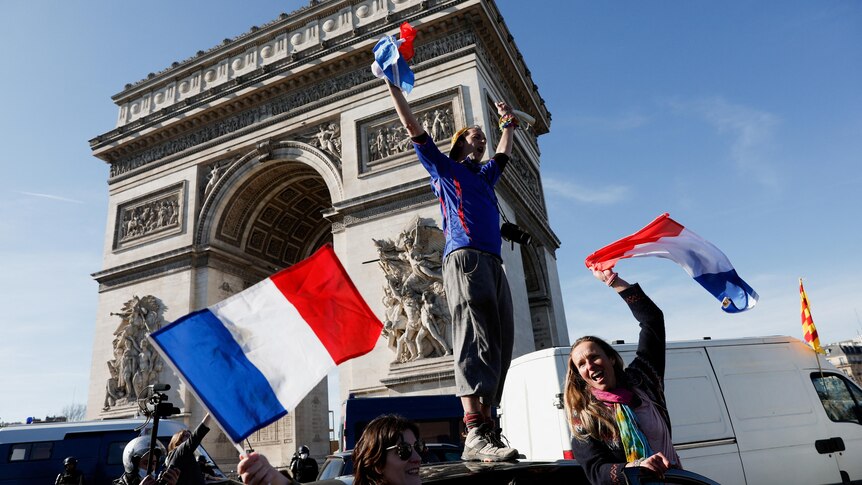 A protester stands atop a vehicle in front of the Arc de Triomphe.