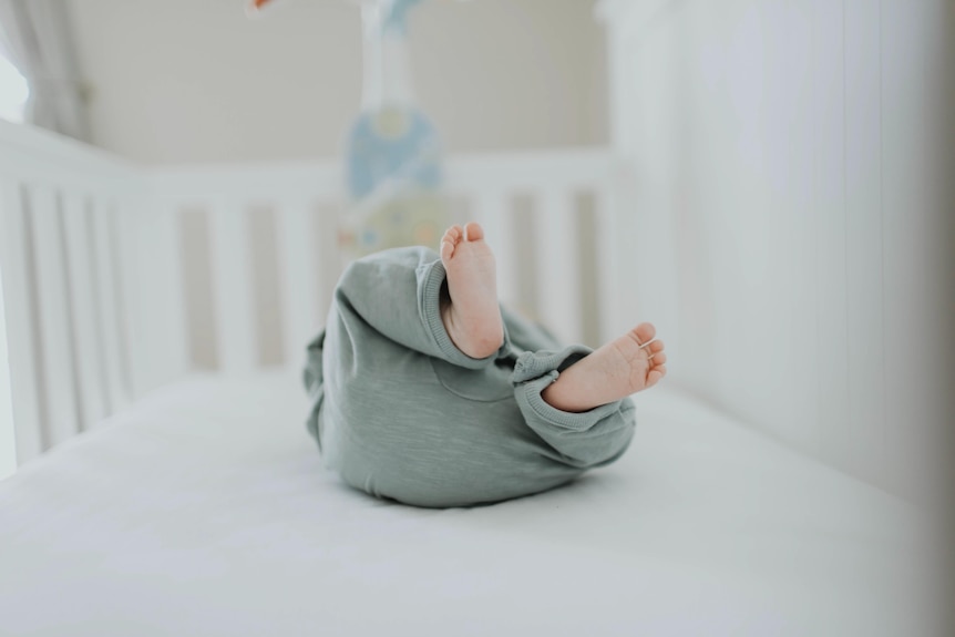 Close-up of baby wearing grey pants lying in cot.