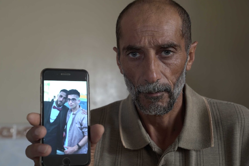 Ali Yusef Jabarin holds a mobile phone displaying a photo of his sons Ehab and Khalil.
