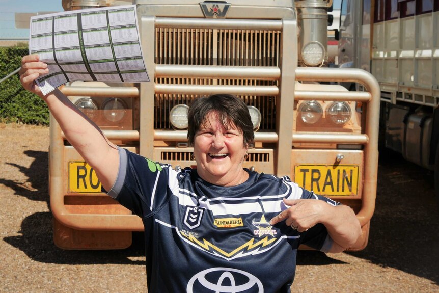 Woman stands in front of road train holding paper wearing football jersey
