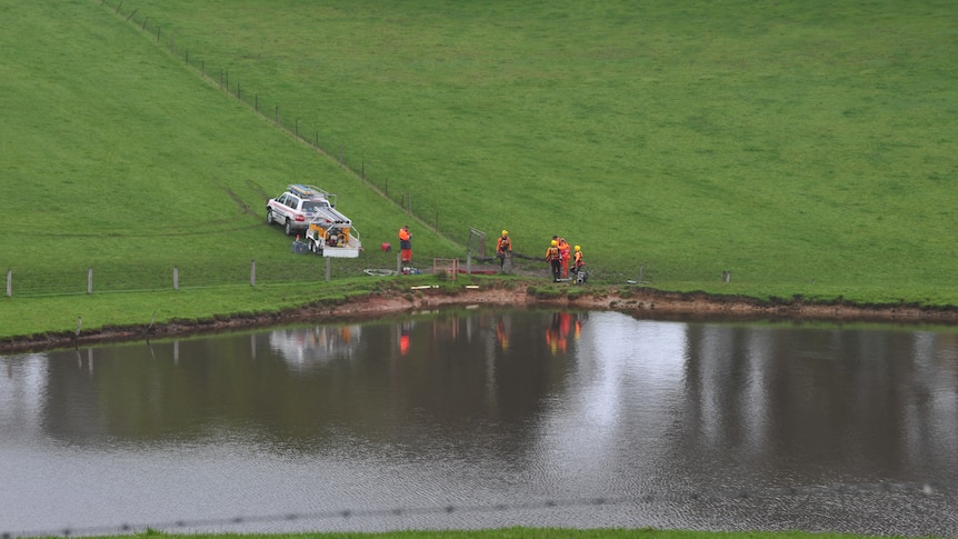 An SES vehicle and volunteers wearing orange coveralls next to a dam.
