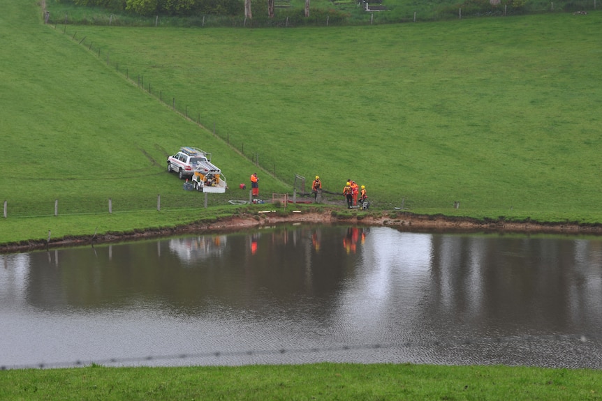 An SES vehicle and volunteers wearing orange coveralls next to a dam.