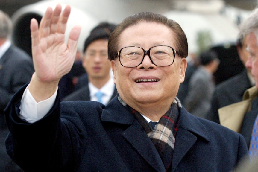 A smiling man waves with his hand in the air. 