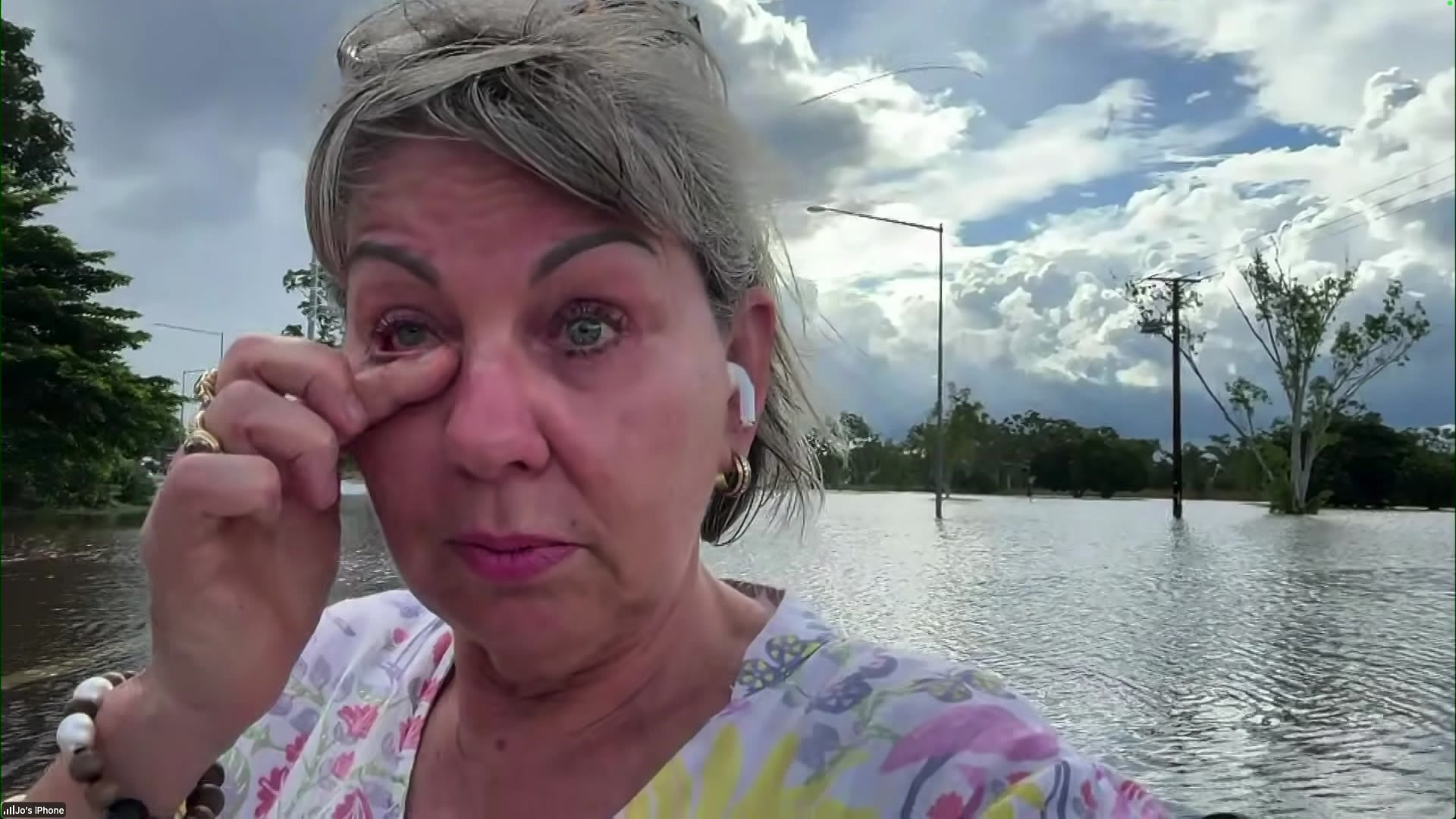A woman wiping tears from her eyes, with floodwaters behind her.