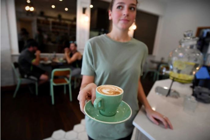 Teenage cafe worker holds cup of coffee in green cup and saucer