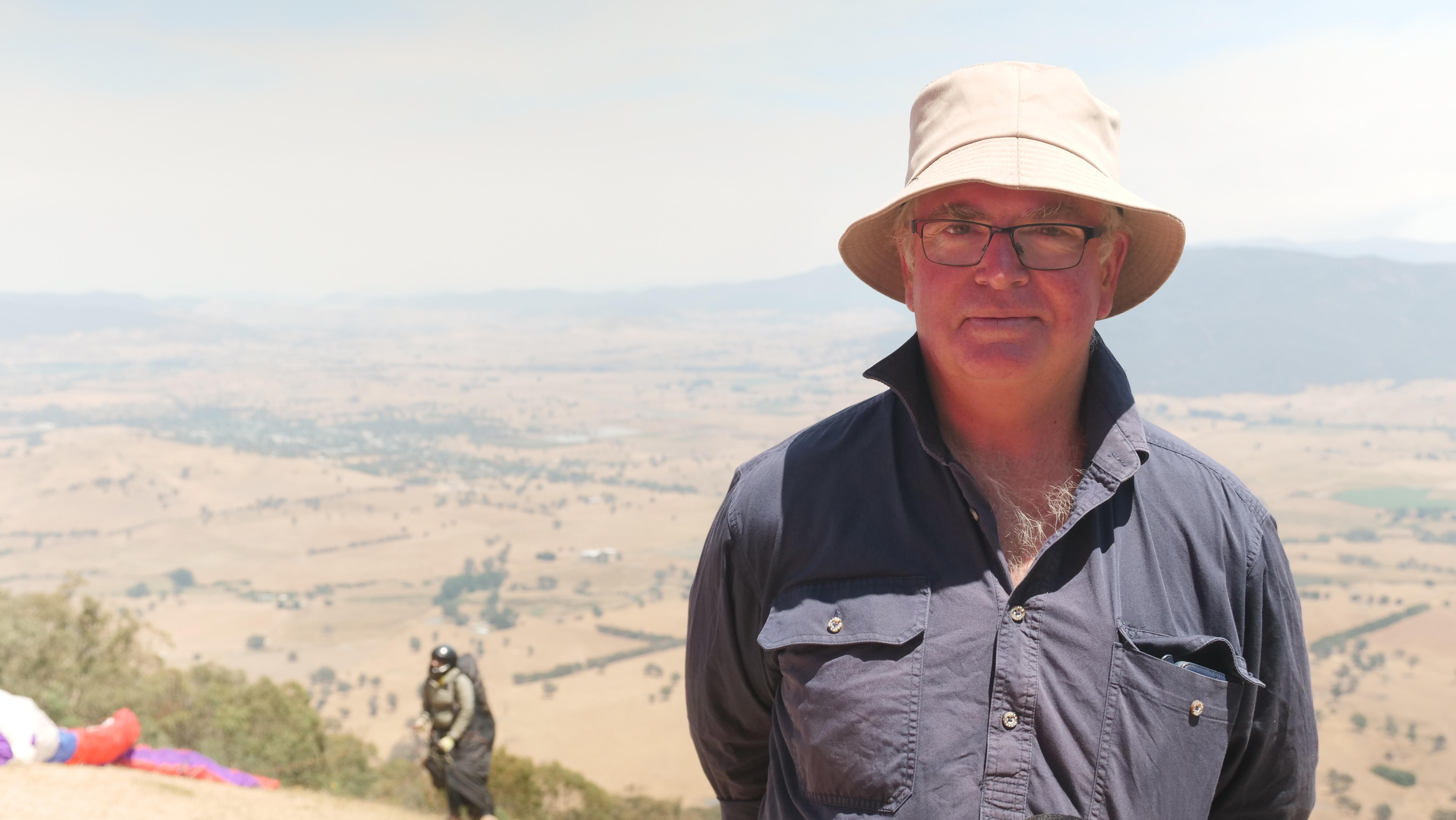 Um homem está em uma montanha com um parapente atrás dele 