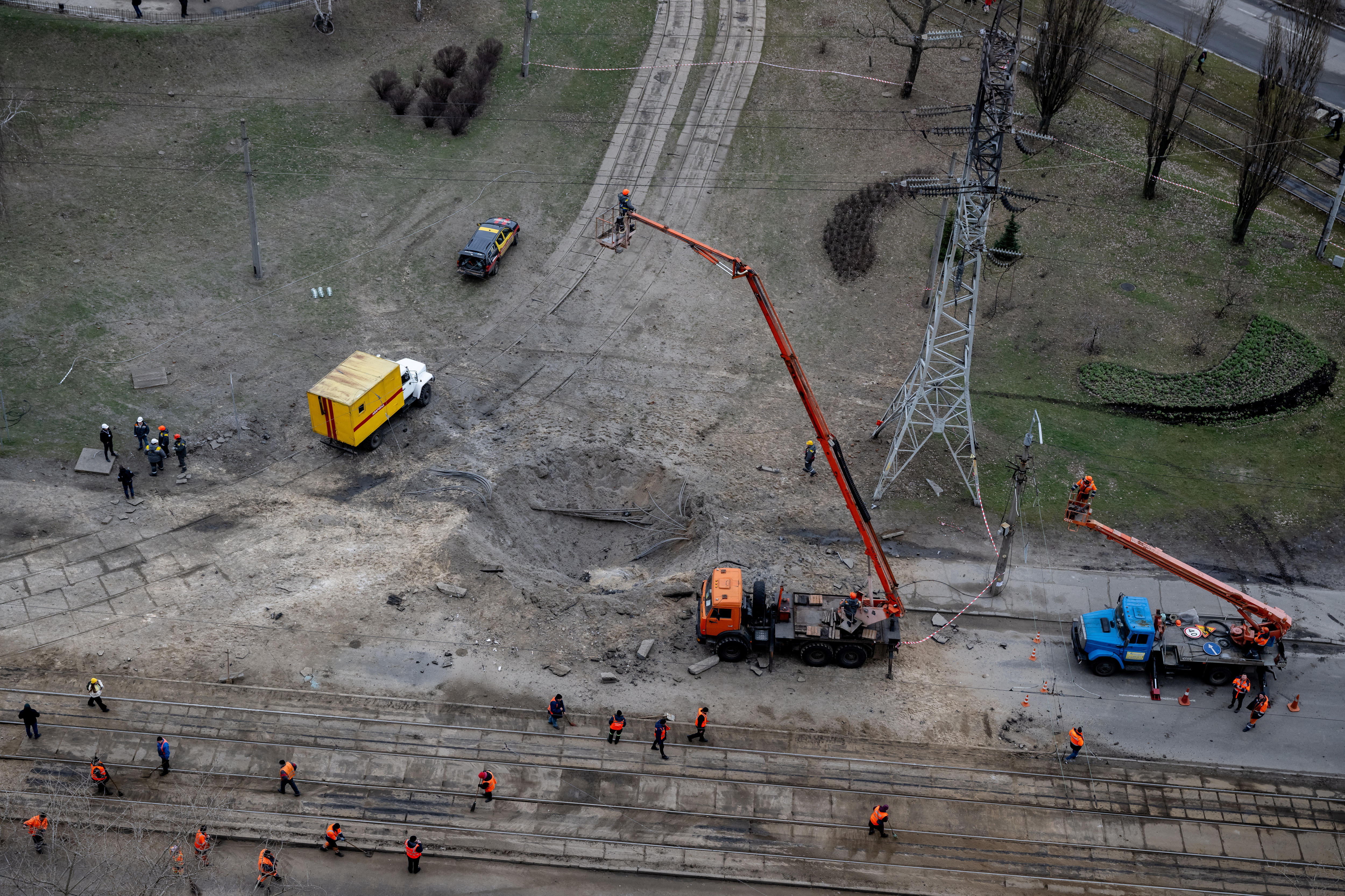 a view of a far away dirt road with a crator in the centre and trucks with cranes and workers surrounding it
