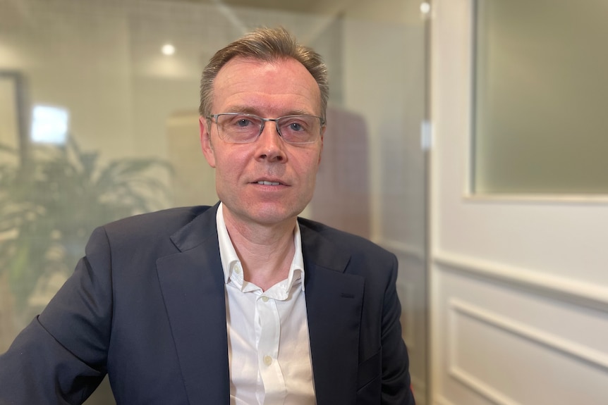 A middle-aged man wearing glasses and a suit in an office