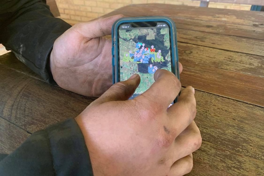 Close-up of a man's hands holding a mobile phone with a map showing several pinned sites 