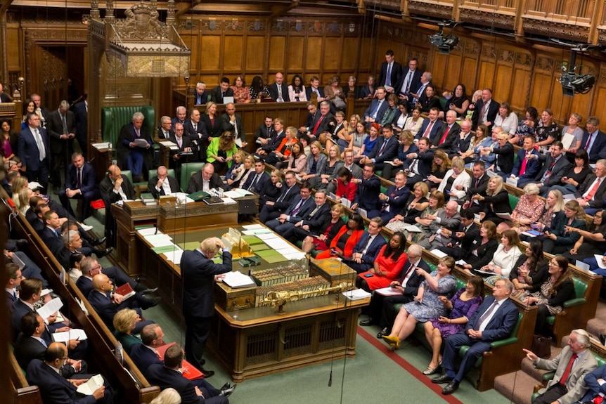 Boris Johnson stands before the House of Commons, which is packed with MPs.