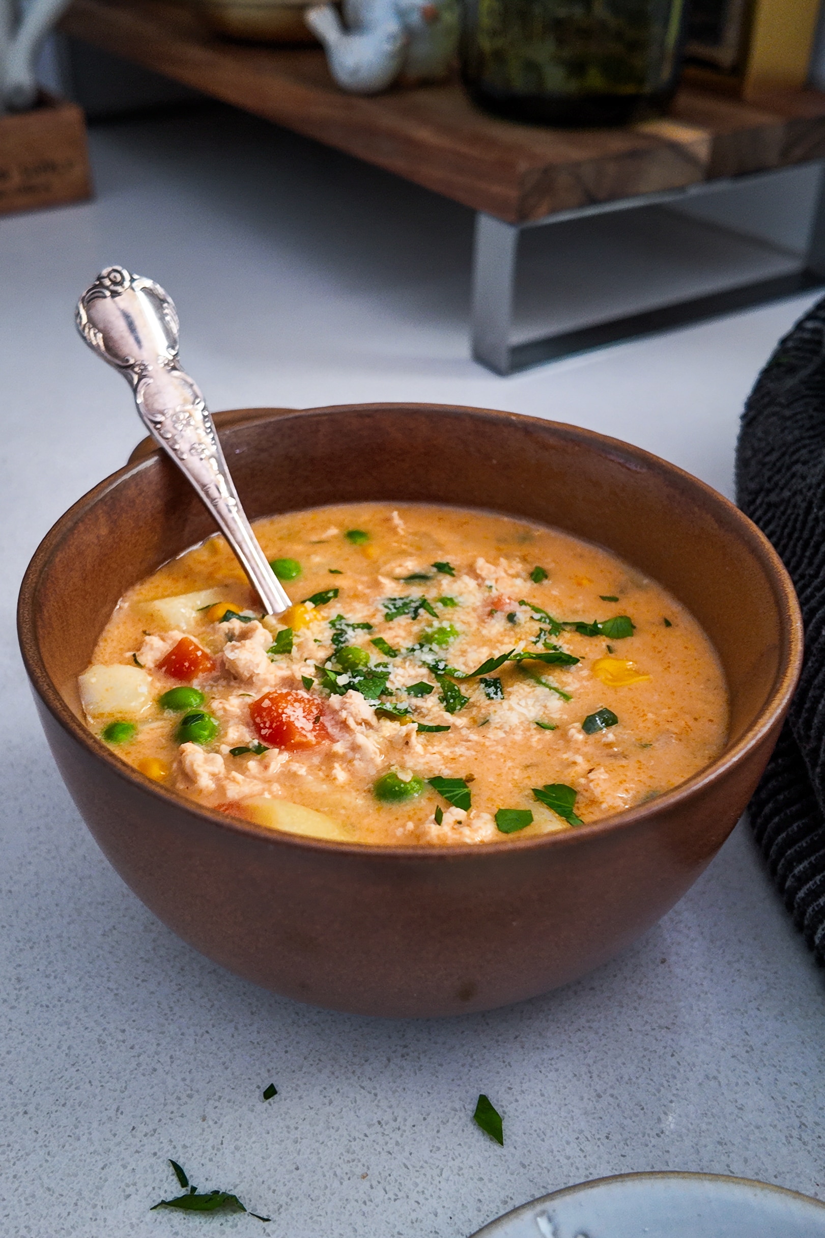 A small bowl of soup, with a spoon in it, sits on a bench.
