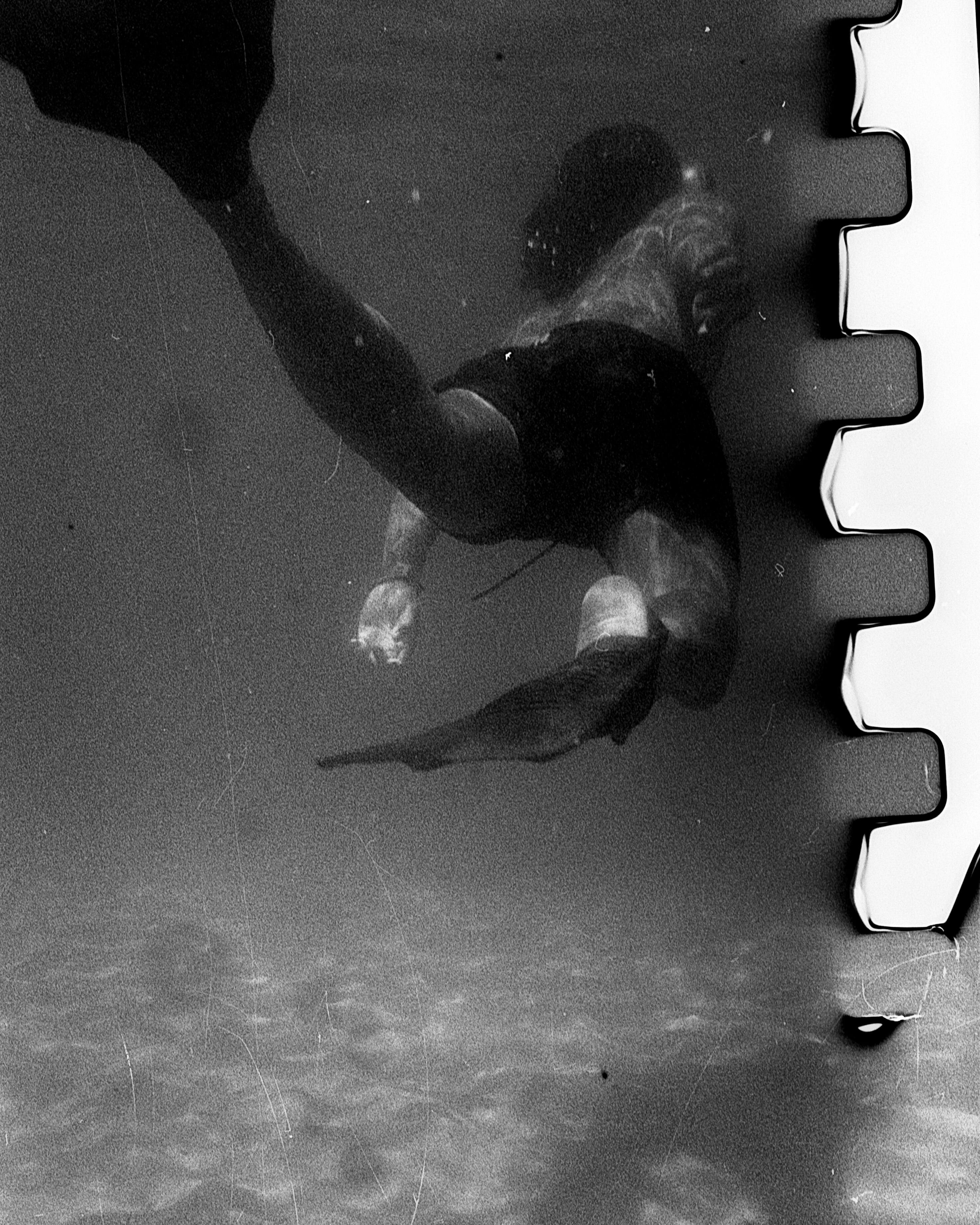 A grainy black and white image of a swimmer underwater 